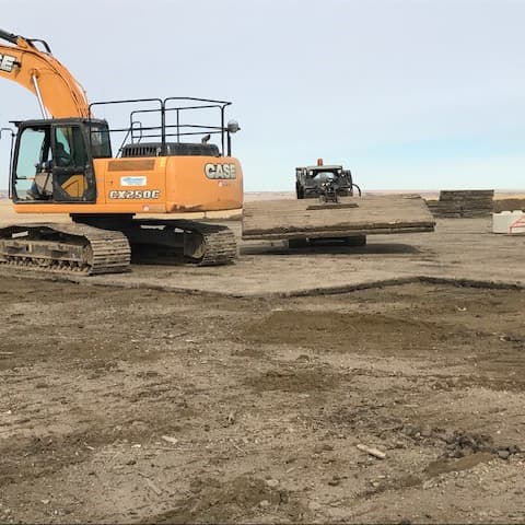 Skidsteer moving mat with excavator to the left.